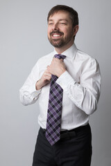 Studio portrait of a caucasian man in his 40s adjusting his purple tie while smiling. He is wearing a white buttoned up shirt and dark dress pants. He is a business executive. 