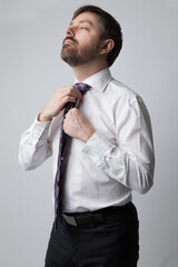 Studio portrait of a caucasian man in his 40s adjusting his purple tie. He is wearing a white buttoned up shirt and dark dress pants. He is a business executive. 