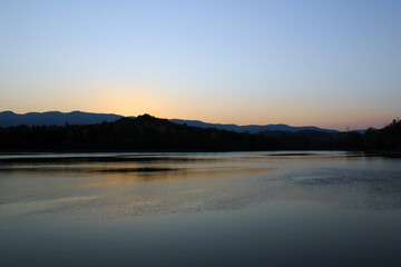 Lake at dusk with dark silhouette of hills on the other side and sky reflection on tghe rippled water surface. Horizontal.