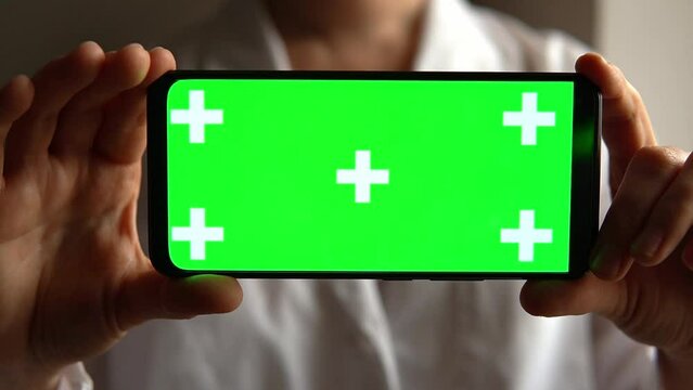Woman doctor holding green screen chroma key smartphone in dark. Layout for mobile applications. Female in medical uniform show app on phone screen. Concept of programs and advertising for medicine