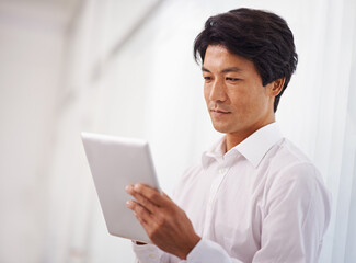Instant access to the companys online database. a handsome asian businessman using his digital tablet in the office.