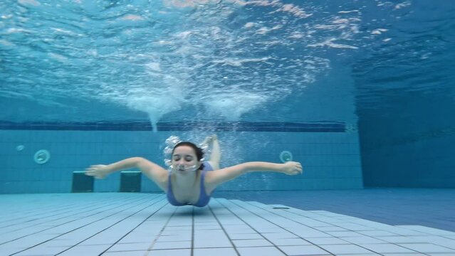 Beautiful girl teenager swimming in pool under water in bikini. Pretty female person diving in blue water at summer and breathe with bubbles