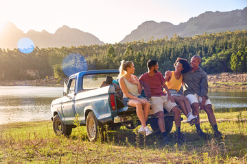 Group Of Friends With Backpacks In Pick Up Truck On Road Trip By Lake And Mountains
