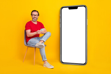 Photo of cheerful funny guy pensioner dressed red t-shirt glasses reading gadget empty space isolated yellow color background