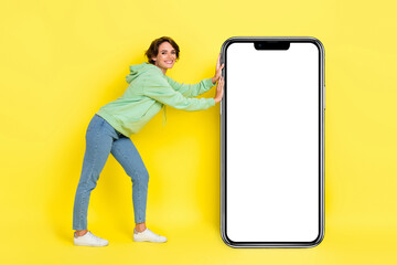 Full length photo of sweet funny lady wear green hoodie reading pushing modern gadget empty space isolated yellow color background