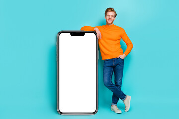 Photo of cool pretty young man wear orange pullover spectacles modern device empty space isolated teal color background