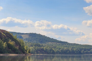 lake surrounded by green forest, hill with forest on background.Summer day