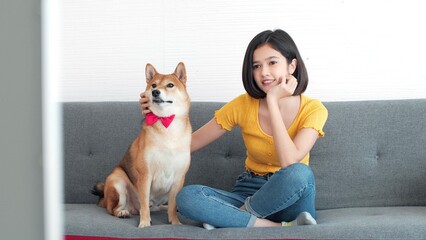 Happy young Asian woman is watching television while her pet puppy cute dog is sitting on sofa at living room