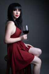 Studio portrait of a beautiful caucasian woman in her 30s wearing a red dress and holding a glass...
