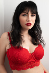 Portrait of a caucasian woman in her 30s wearing a red lace bra and red lipstick. She has black hair with bangs. This is Valentine's Day themed portrait. 