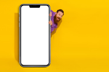 Full length photo of funky positive man peeking behind empty space big screen isolated on yellow color background