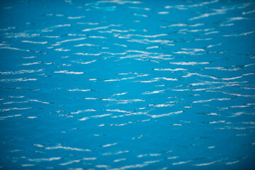 Water background. Blue water, ripples and highlights. Texture of water surface and tiled bottom.