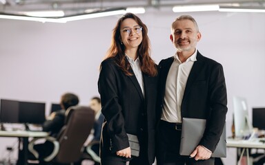 Happy business partners with folder posing together. Smiling businesswoman and businessman standing...