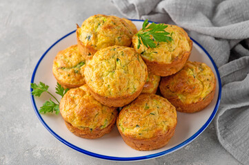 Homemade zucchini muffins with cheese, garlic and herbs on a plate on a gray concrete background....