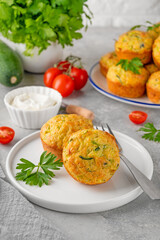 Homemade zucchini muffins with cheese, garlic and herbs on a plate on a gray concrete background. Vegetarian dish. Copy space.