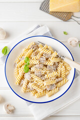 Fusilli pasta with mushrooms, cheese and fresh basil in a plate on a white wooden background.