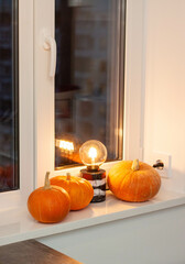 Cosy autumn still life with pumpkins and retro lamp on the windowsill. Dark evening, warm light and calm mood