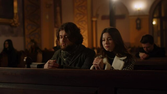 A married couple listens to a sermon at a Sunday service in a Catholic church. Husband and wife sitting on the bench attentively listening to the sermon of the priest.