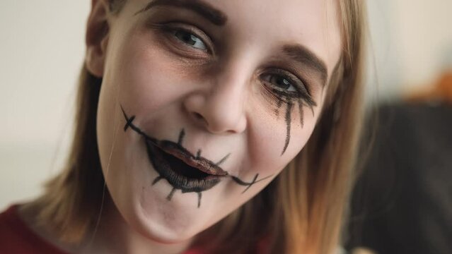 Preteen girl with spooky Halloween makeup posing at camera closeup portrait. Child kid acting for creepy holiday