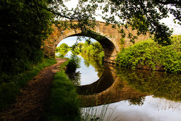 Fototapeta na wymiar A stunning landscape shot of a bridge over the Leeds and Liverpool canal. The reflection of the bridge can be seen in the water below.