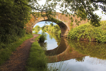 Fototapeta na wymiar A beautiful scenic and postcard shot of a bridge crossing over the Leeds to Liverpool Canal, the reflection of the bridge clearly visible in the water.