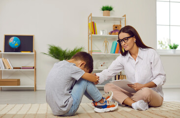 Frustrated sad confused teen boy sitting on floor in closed pose near the school psychologist....