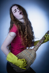 Maid cleaning service concept. Young beautiful female cleaner has fun with broom as if she is a rock musician.