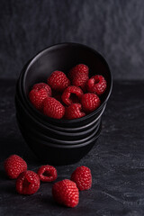 Ripe raspberries in black bowl on  dark background. Selective focus.