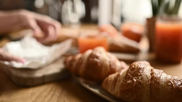 French breakfast with croissants and brie cheese at sunny kitchen. Hands open camembert package and delicious bakery pastry