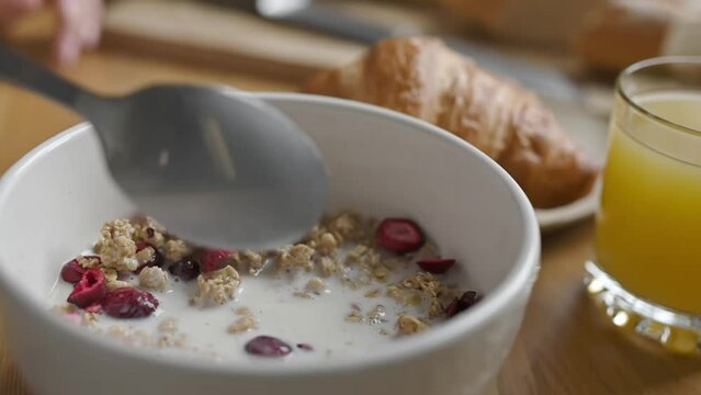 Girl stearing oatmeal with fruits and berries in bowl plate for delicious cereal breakfast at kitchen. Woman preparing granola with latte for morning healthy diet meal