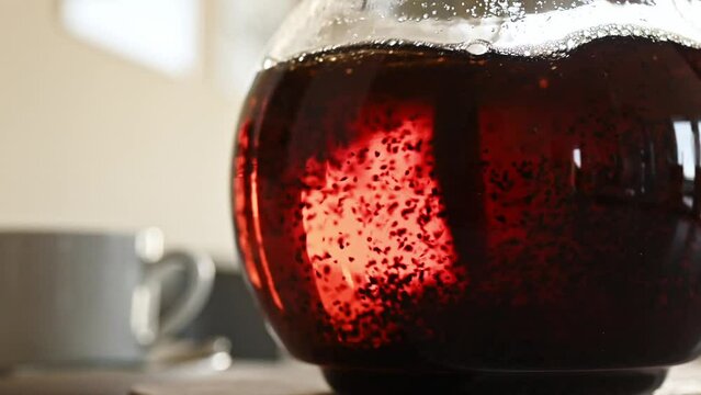 Person stirs black tea in transparent teapot with spoon closeup. Kettle with hot natural beverage at kitchen