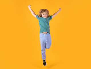 Energetic kid boy jumping and raising hands up on isolated studio background. Full length body size photo of jumping high child boy, hurrying up running fast on yellow background.