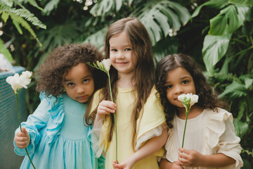 Three little girls in the garden with flowers in their hands. children of different nationalities.
