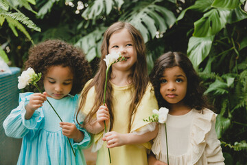 Three little girls in the garden with flowers in their hands. children of different nationalities.