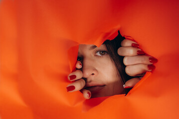 Surprise. Portrait of a young caucasian woman looking through the hole in white paper. Distrustful...