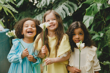 Three little girls in the garden with flowers in their hands. children of different nationalities.