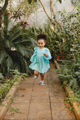 A little girl in a white dress runs along the path in the botanical garden.