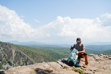 A man sitting on a mountain with a backpack looks inside a bag putting things in a backpack, hiking...