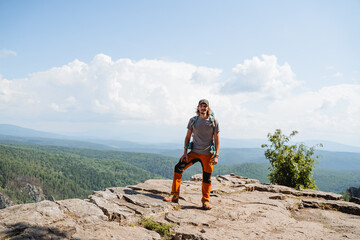 Fototapeta premium A tourist stands on top of a mountain looking into the camera, a guy with a backpack climbed a cliff, a place to camp in the mountains, a hipster on a hike, a trip to Europe