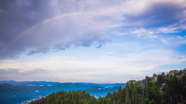 Multi-colored rainbow flaunts on top of the Rhodope Mountains above intermountain valley with the village of Smolyan
