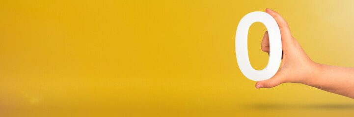 Numeral zero in hand. A hand holds a white number zero on a yellow background with copy space. Zero concept, 0 percent interest rate, minimum air emissions, cost or credit no increase.