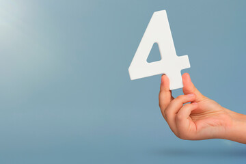 number four in hand. Hand holding white number 4 on blue background with copy space. Concept with...
