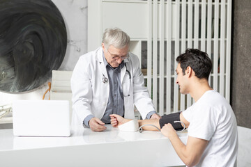 Senior doctor is measuring with tonometer blood pressure of his young patient in modern medical office