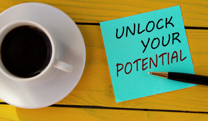 UNLOCK YOUR POTENTIAL - words on a green sheet on a yellow wooden background with a pen and a cup of coffee