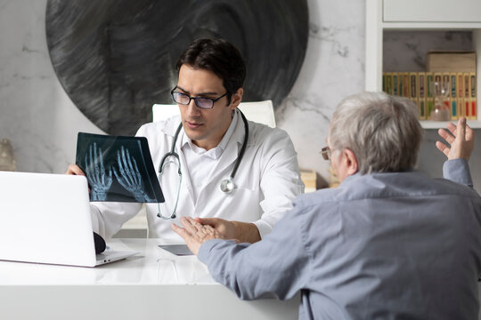 Old man visiting young male doctor rheumatologist in modern clinic