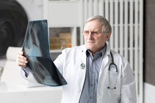 Aged doctor holds x-ray image of lungs in modern medical office