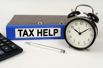 On a white surface, an alarm clock calculator and a folder with the inscription - Tax help