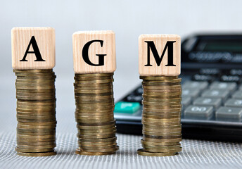 AGM - acronym on wooden cubes on the background of coins and calculator