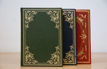 Green, blue and red cover vintage books bound in leather stacked on the bookshelf