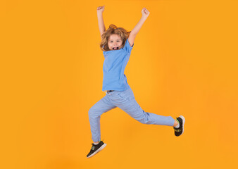 Fototapeta na wymiar Full length of excited kid jumping. Energetic kid boy jumping and raising hands up on isolated studio background. Full length body size photo of jumping high child boy, hurrying up.